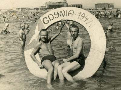 Plaża gdyńska – dwóch młodych mężczyzn na drewnianym kole w wodzie